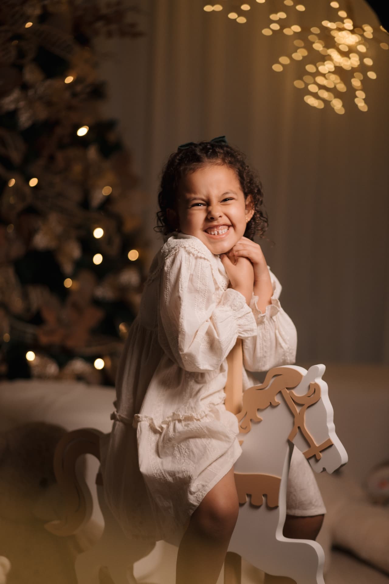 Menina sorrindo junto ao cavalinho de madeira, diante da árvore de Natal