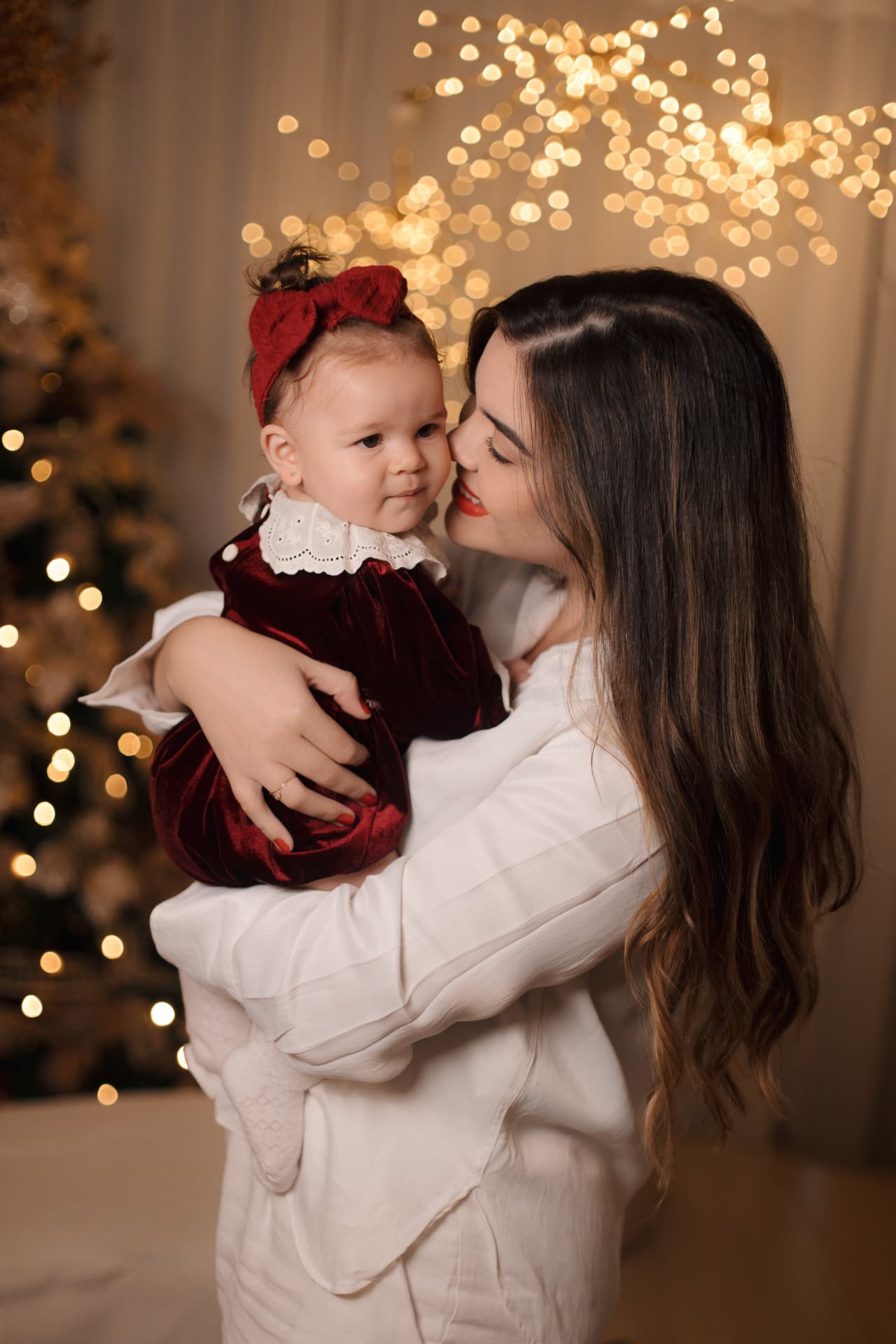 Mãe beijando a filha com laço vermelho