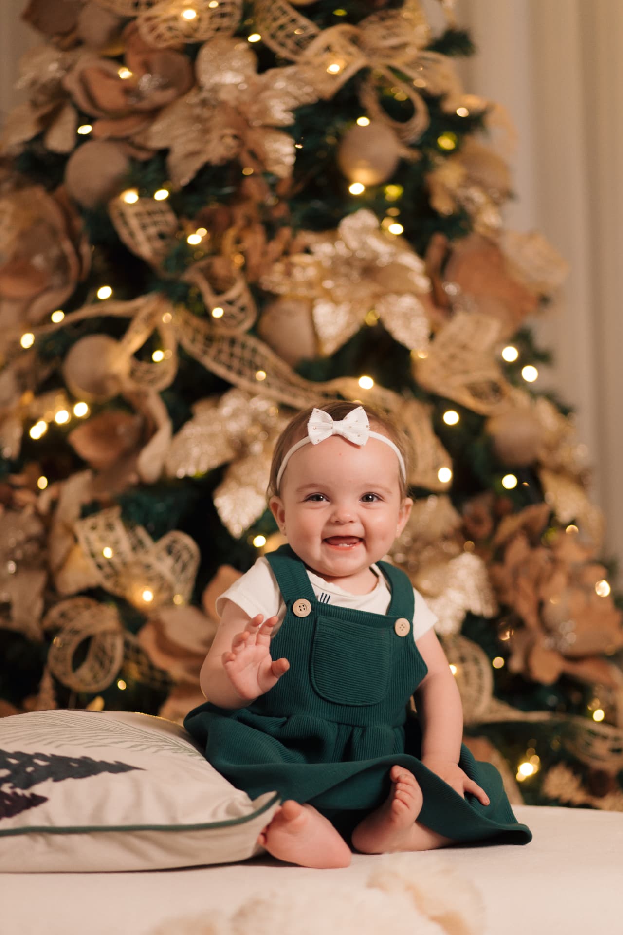 Bebê de vestido verde diante da árvore de Natal